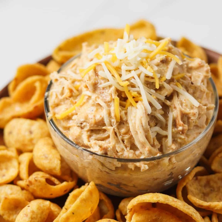 crock pot mexican chicken with shredded cheese on top sitting on plate of corn chips
